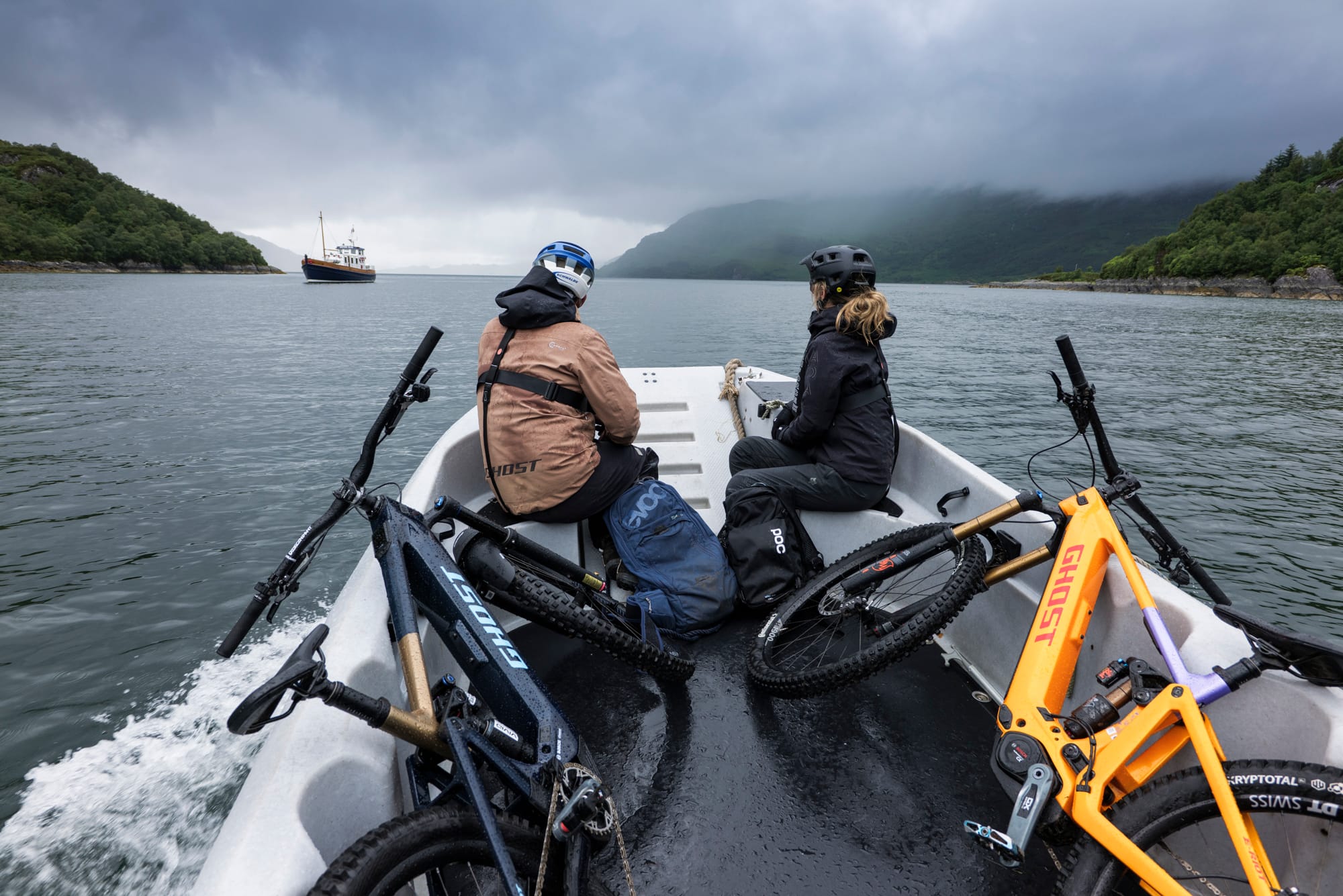 Two mountain bikers on a boat with bikes, showcasing Ghost E-Riot Photo and Video Production in a scenic landscape. - Alexi Hall