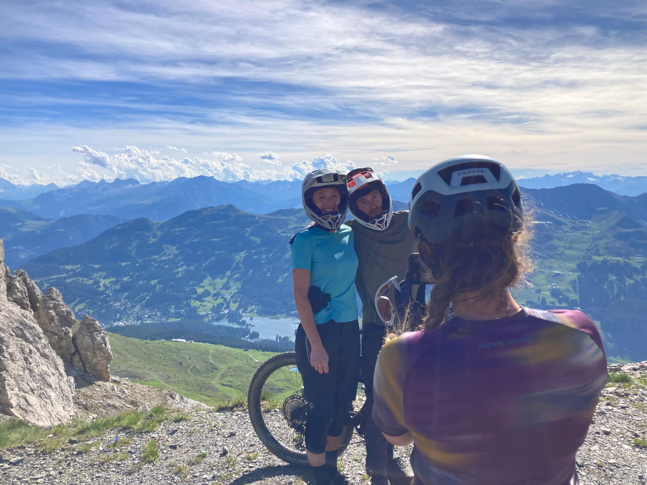 Mountain bikers wearing helmets pose for a photo against a stunning mountain backdrop, showcasing MTB helmet content production. - Alexi Hall